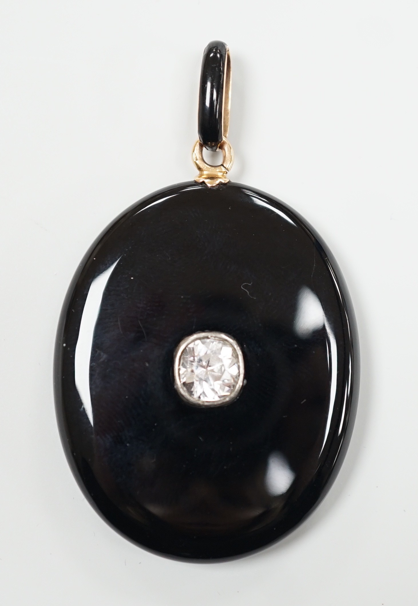 A Victorian yellow metal mounted black onyx oval locket, with black enamelled bale and set with an old cut white sapphire, overall 62mm